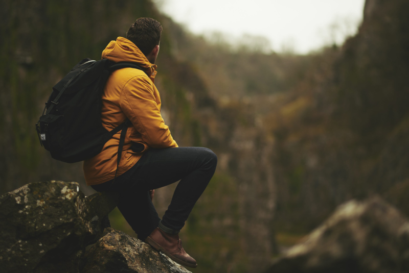 PRP for osteoarthritis of the knee - A man in a yellow raincoat with a rucksack on, sitting on a rock looking away from the camera