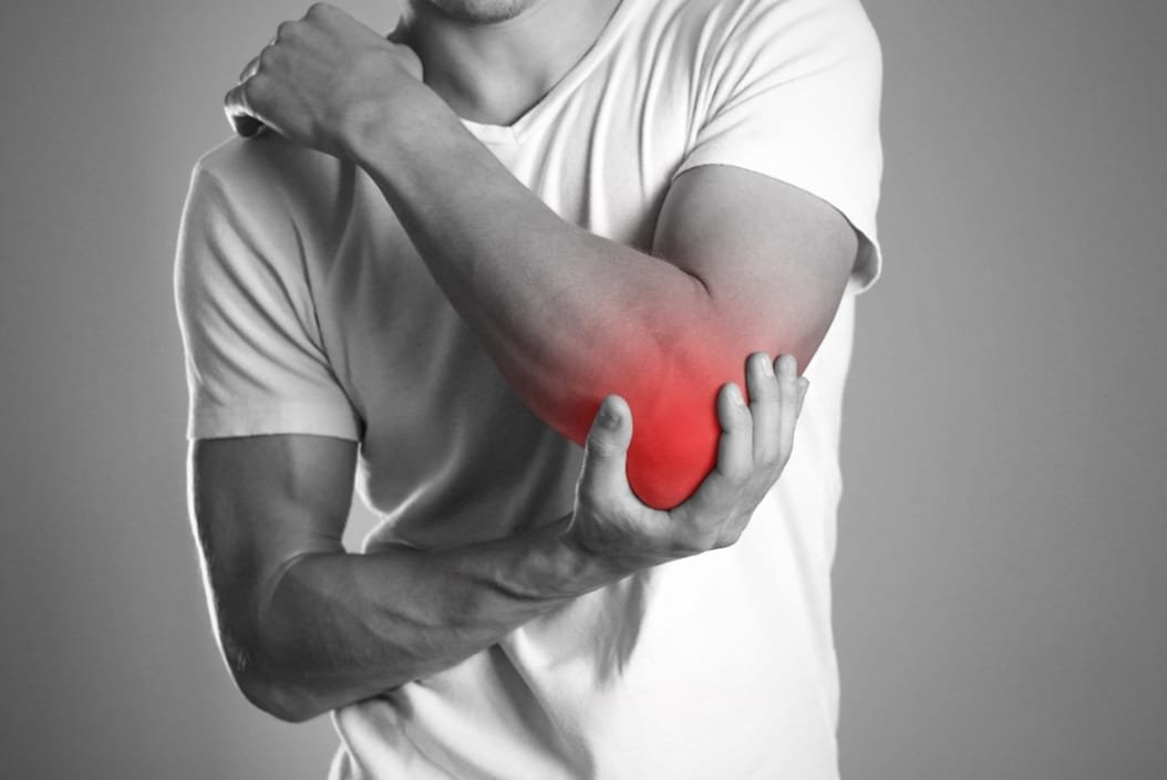 Tennis elbow - Front of a male wearing a white t-shirt in black and white colour holding his left elbow with his right hand.