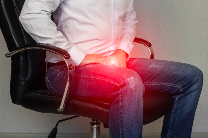 iliopsoas tendinopathy - a man sat at an office chair with hands holding hips