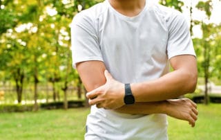 Distal biceps tendon - A man in a white t-shirt holding his right elbow with his left hand.