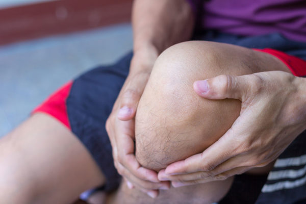 patella tendinopathy - athlete holding knee in pain with patellar tendinopathy